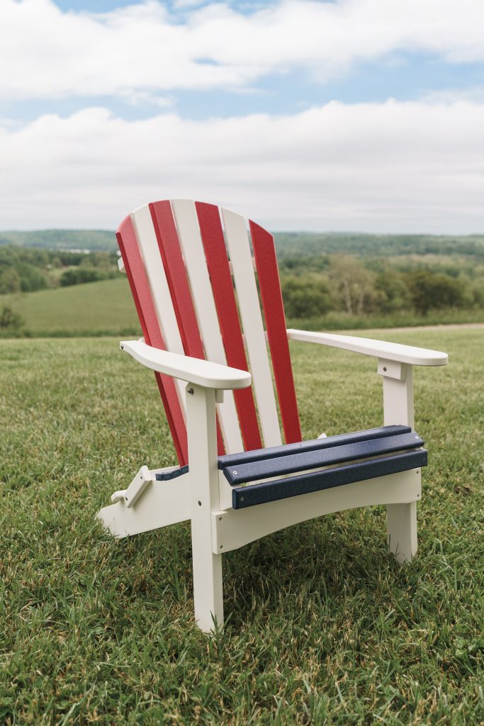 Red-and-white striped Adirondack chair on a grassy field with rolling hills and a blue sky in the background.